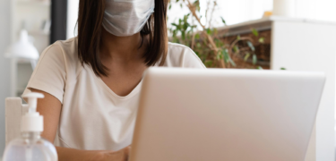 A woman wearing a mask works on her laptop.