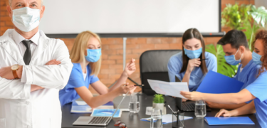 Students in scrubs and wearing masks investigate a document together.