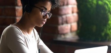 A young woman wearing headphones uses her laptop.