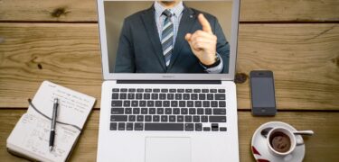 On a laptop screen, a man in a suit is pointing.