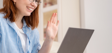 A woman waves at her laptop.