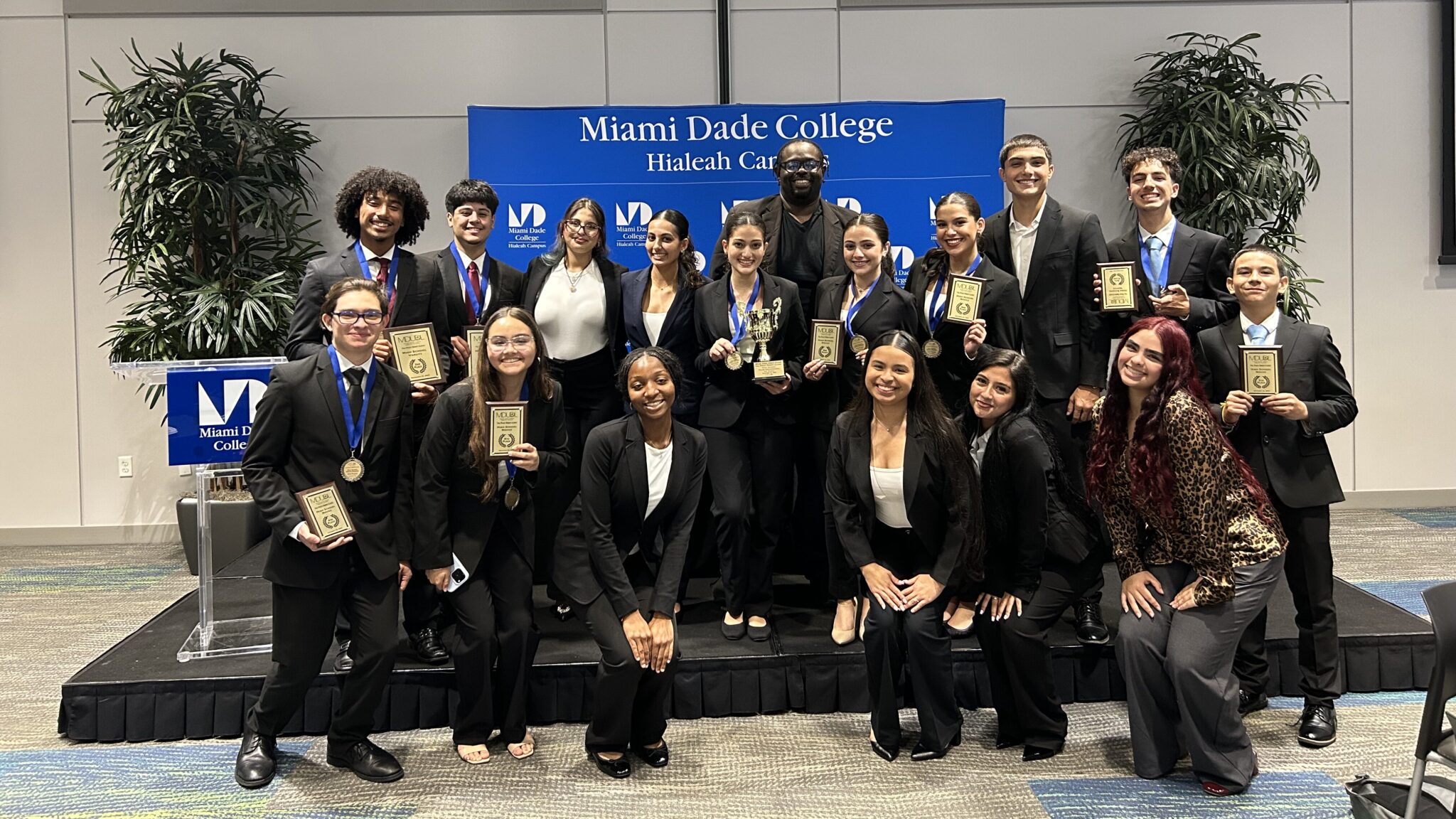 A group of NAF Academy of Law of students in formal attire stand proudly holding plaques and medals at an award ceremony at Miami Dade College.